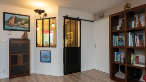 A room with a sliding door, a bookshelf, a framed painting, and a wooden cabinet. - Holiday Home 'Upton 2 - Arradon Golfe Du Morbihan' with Private Terrace, Garden & Wi-Fi (Arradon)