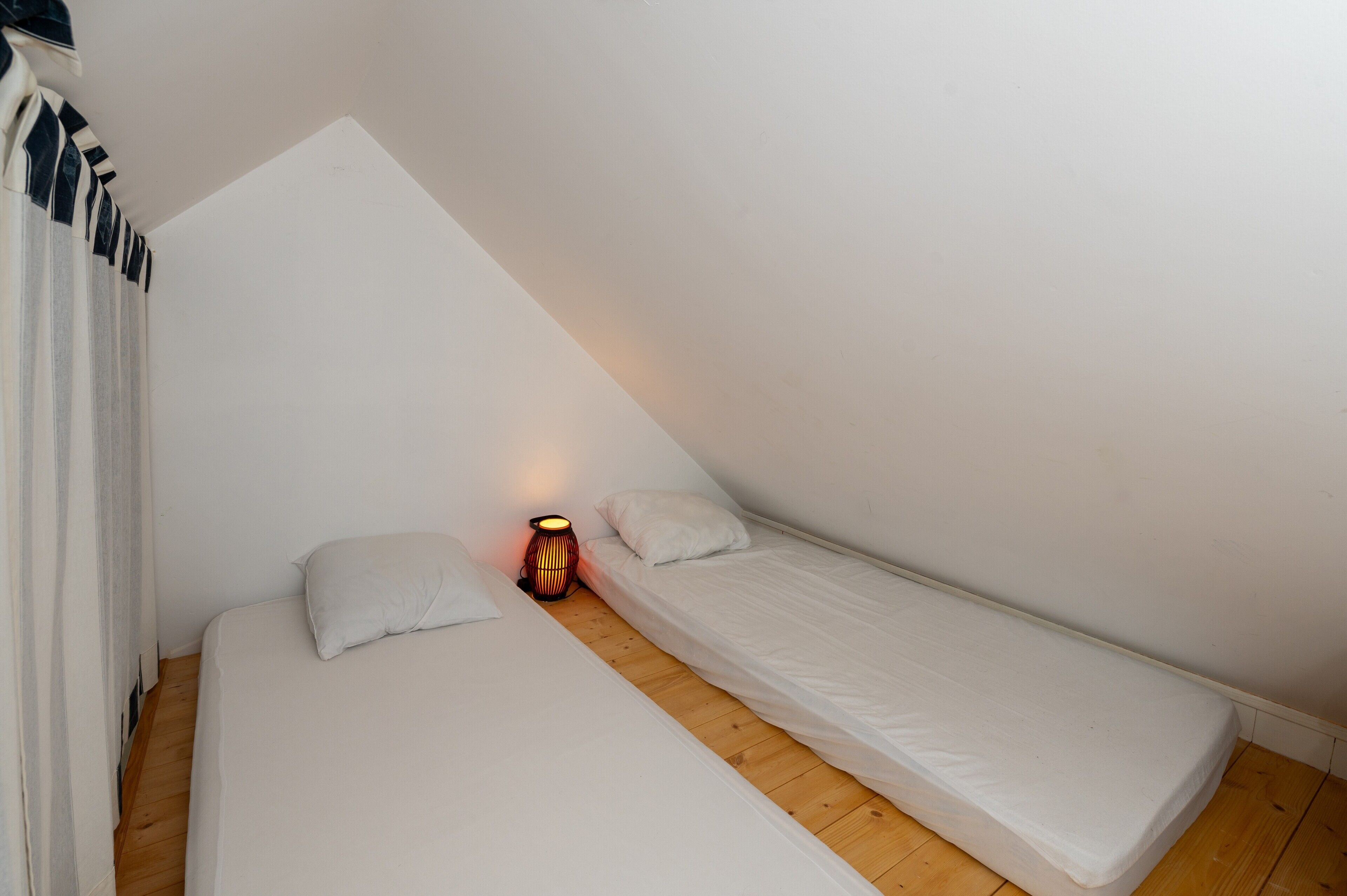 Una habitación pequeña con una cama individual, techo inclinado, lámpara de noche y suelo de madera.
