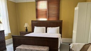 Une chambre à coucher avec un grand lit, un banc, une chaise, une table de chevet et un ventilateur de plafond.