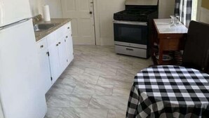 Une cuisine compacte avec des meubles blancs, une cuisinière et un coin repas agrémenté d’une nappe à carreaux.