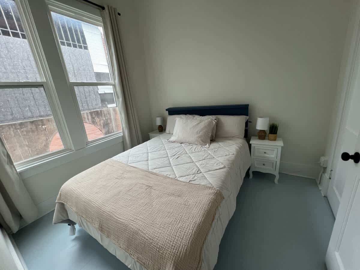 A bedroom with a bed, a nightstand, a lamp, and a window.