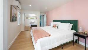 A bedroom with a large bed, a bedside table with a lamp, and a door leading to another room.