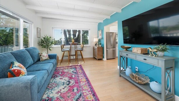 A modern living room with a blue sofa, a dining table, and a kitchen area with a large TV.