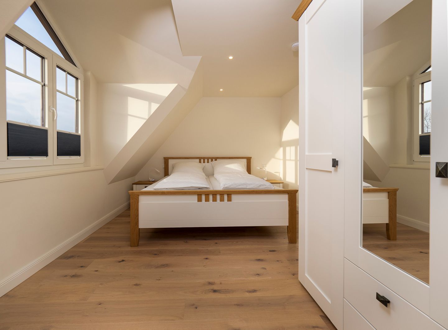 A bedroom with a sloped ceiling, a bed, a nightstand, and a dresser.
