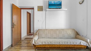 Une pièce comprenant un canapé, un téléviseur posé sur un meuble, une porte et un luminaire fixé au mur.