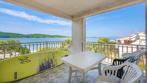Un balcon avec une table et des chaises, une planche de surf et une vue sur un lac et des collines.