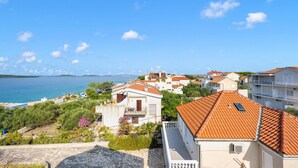 Une ville côtière aux bâtiments aux toits de tuiles rouges, sous un ciel bleu azur, offrant une vue sur la mer.