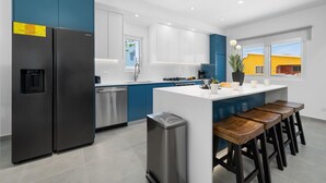 A modern kitchen with stainless steel appliances, a central island with bar stools, and a view of the outside.
