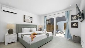 A modern bedroom with a large bed, a nightstand, a TV mounted on the wall, and a sliding glass door leading to a balcony.