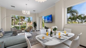 A modern living room with a grey sofa, a dining table set for breakfast, and a TV mounted on the wall. - Eagle Beach Resort Ground Level 3BR2BA Pool Levent (Oranjestad)