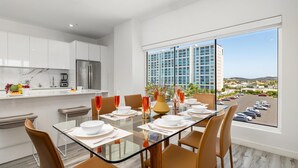 Un espace repas moderne avec une table en verre, des chaises marron et une vue sur des immeubles de grande hauteur.