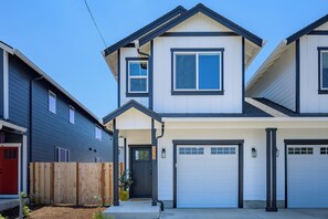 A two-story residential building with a garage, a front door, and a small porch.