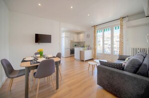 Een moderne woonkamer met een grijze bank, een eettafel gedekt voor vier personen, en een keuken op de achtergrond.