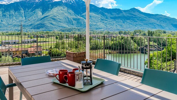 A terrace with a table set for two, overlooking a mountainous landscape and a river. - Lovely apartment for 4 guests with WIFI, terrace and panoramic view (Gera Lario)