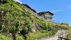 A stone staircase leading to a stone building with balconies, surrounded by lush greenery and pink flowers. - Lovely apartment for 4 guests with WIFI, terrace and panoramic view (Gera Lario)