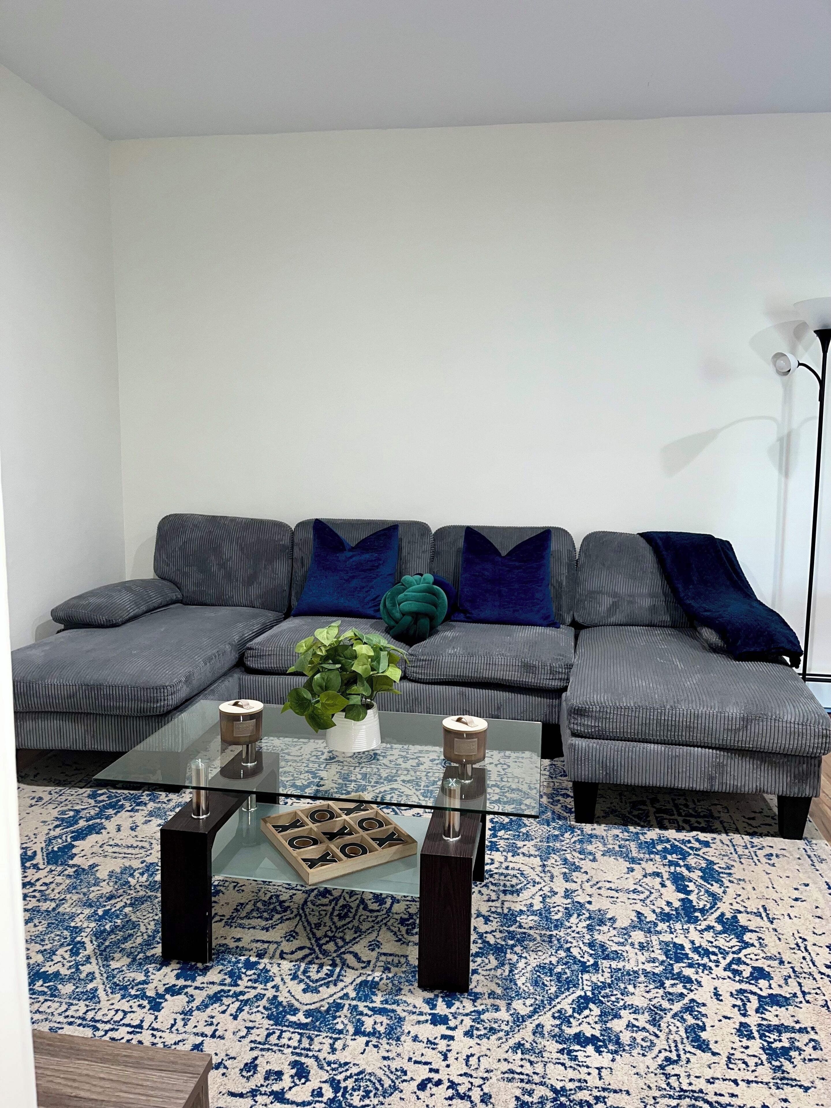 A living room with a sectional sofa, a glass coffee table, and a patterned rug.