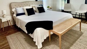 Une chambre à coucher moderne avec un grand lit, des tables de chevet, une chaise et des œuvres d’art accrochées aux murs.