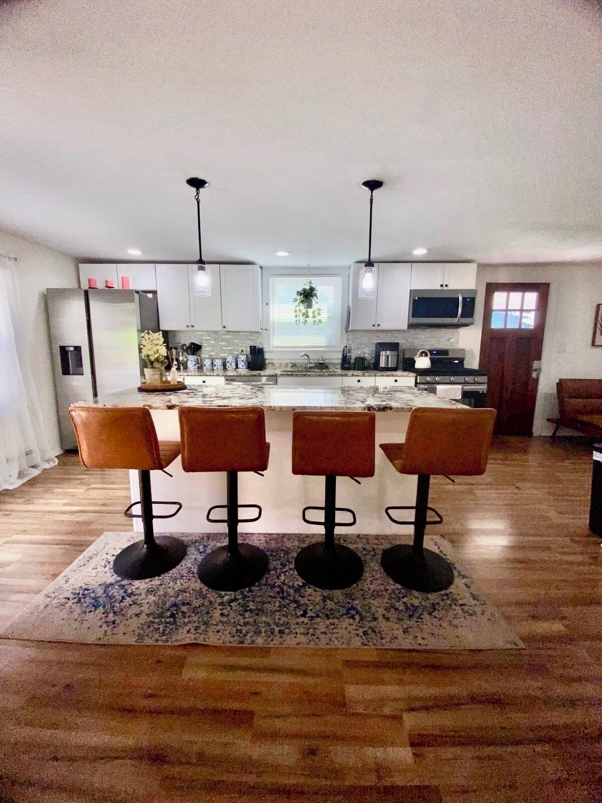 A modern kitchen with white cabinets, a central island with bar stools, a microwave, and a stove.
