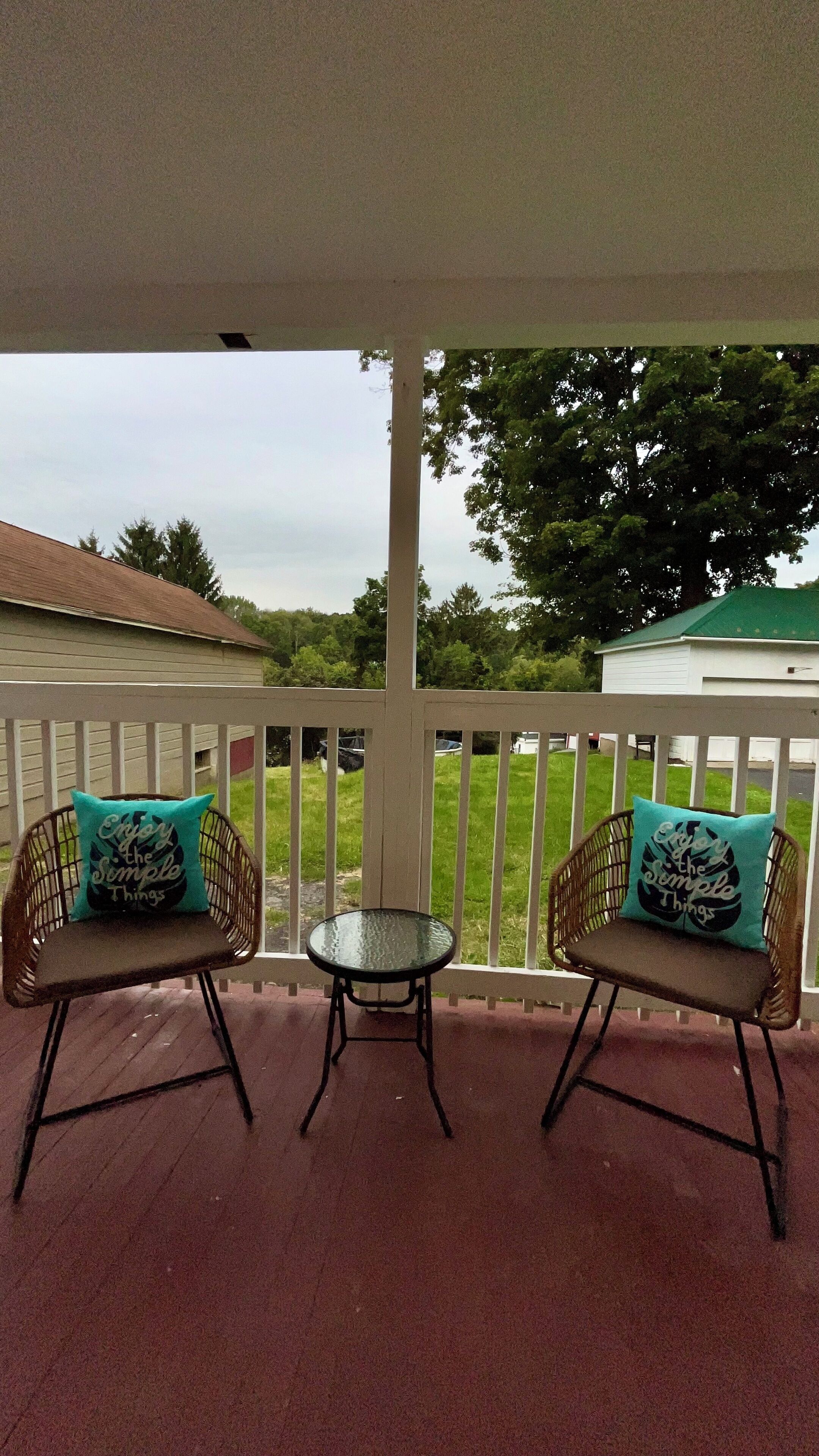 A covered porch with two wicker chairs and a small table, each with a teal cushion.