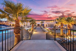 A pathway leading to a pool area with palm trees and a sunset sky.