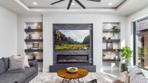 A modern living room with a fireplace, a sofa, a coffee table, and shelves with decorative items. - Desert Sands at Pecan Valley Resort  (Hurricane)