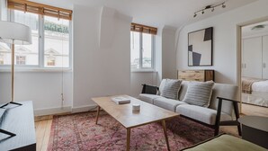En moderne stue med en sofa, et sofabord og en lampe. Der er vinduer med persienner, et tæppe og et billede i ramme på væggen.