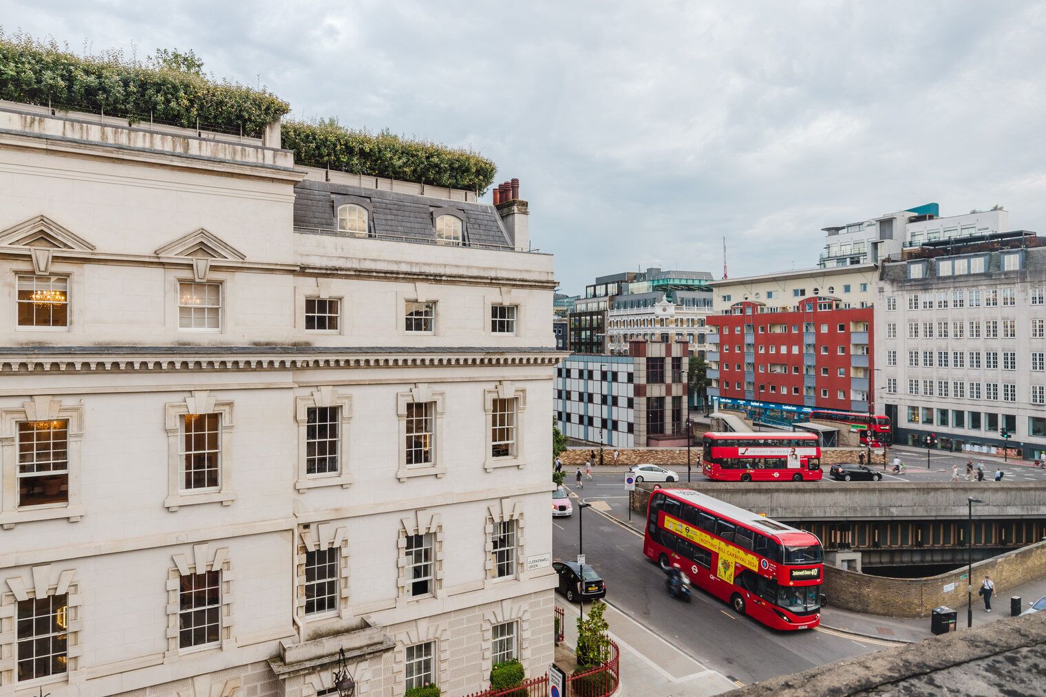 A city street with a red double-decker bus, buildings with classical architecture, and a clear sky.
