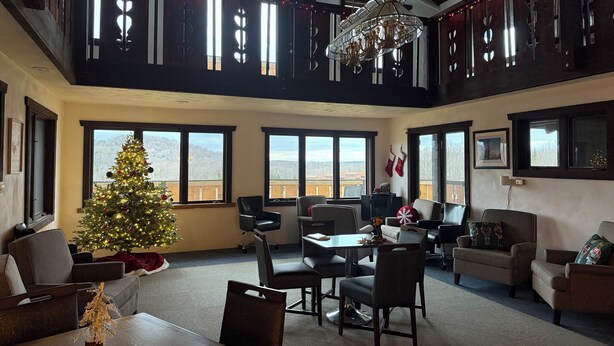 A spacious living room with a large Christmas tree, multiple windows, and a high ceiling with exposed beams. - Davos Chalet (Upson)