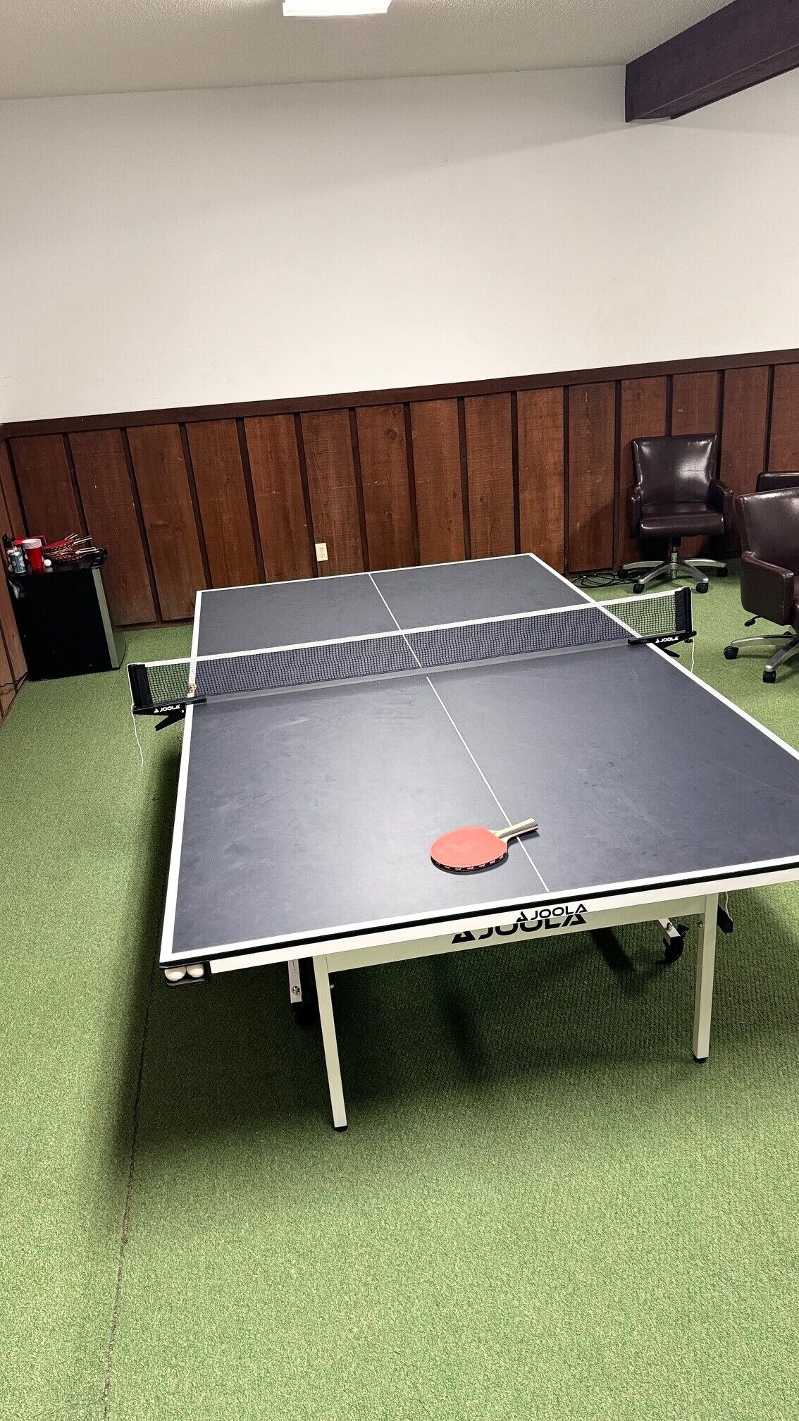 Une table de ping-pong avec un filet, une raquette rouge et une lampe de table.