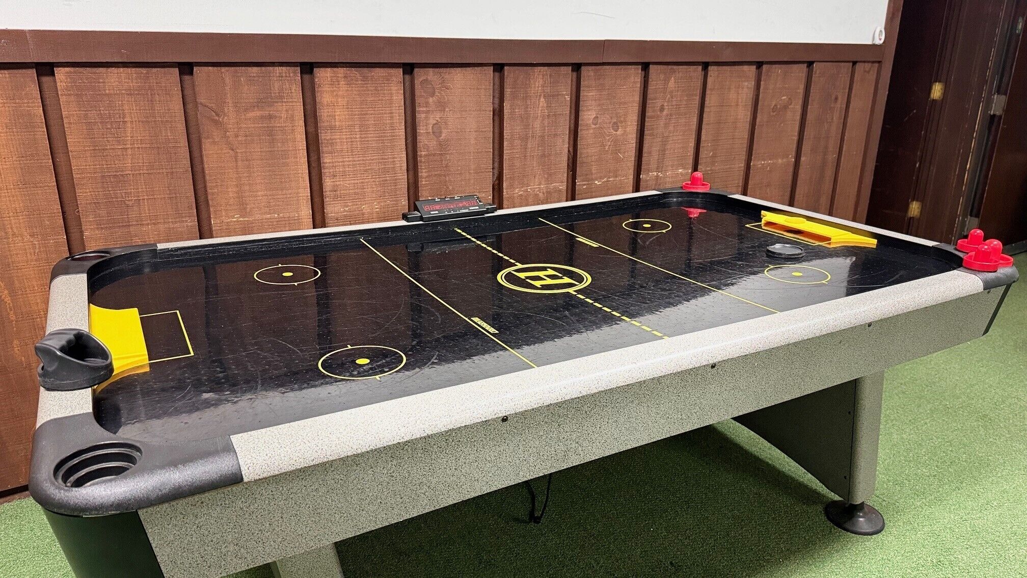A foosball table with a black and white surface, yellow and red player figures, and a wooden backdrop.