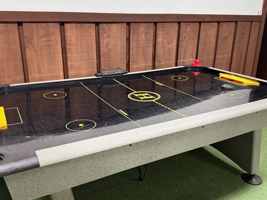 A foosball table with a black and white surface, yellow and red player figures, and a wooden backdrop.