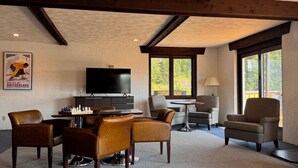 A cozy living room with a fireplace, a television, a chessboard, and a large window offering a view of the outdoors. - Davos Chalet (Upson)