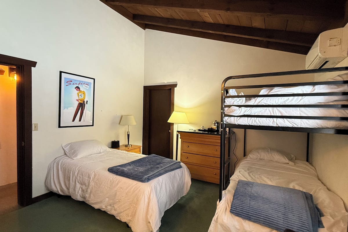 A room with two single beds, a wooden dresser, a framed picture on the wall, and a ceiling fan.