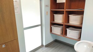 A bathroom with a sink, wooden shelves with laundry baskets, and a door with a frosted glass panel. - Hotel Sunrise (Onagawa)