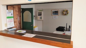 A reception desk with a sign, a green door, a wall-mounted information board, a framed picture, and a wreath. - Hotel Sunrise (Onagawa)