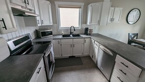A modern kitchen with white cabinets, a stainless steel dishwasher, a microwave, and a built-in oven. - Peaceful and Inviting 4 Bedroom Bilevel House  (Red Deer)