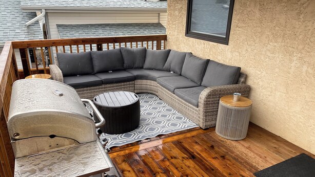 A covered outdoor seating area with a sectional sofa, a round table, and a grill. - Peaceful and Inviting 4 Bedroom Bilevel House  (Red Deer)