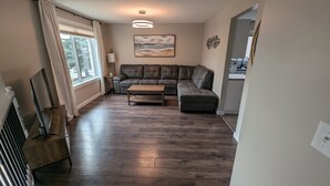 A living room with a dark wood floor, a leather sofa, a wooden coffee table, and a painting of a beach scene on the wall. - Peaceful and Inviting 4 Bedroom Bilevel House  (Red Deer)