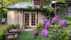 A house with a front porch, a wooden table and chairs, and a garden with purple flowers. - Cosy bespoke Cottage in Olinda-central location (Olinda)