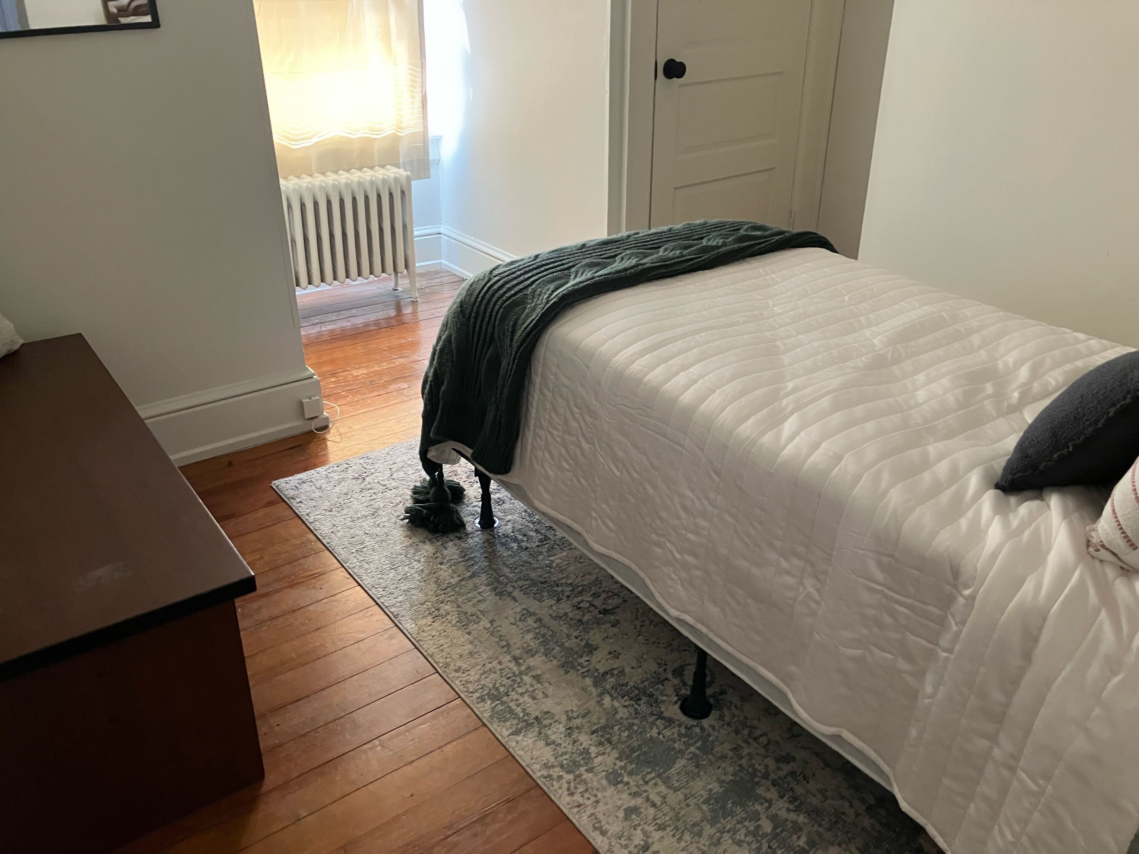 Une chambre à coucher avec un lit, un plancher en bois, un radiateur et une porte.