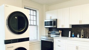 A modern kitchen with a built-in washer and dryer, stainless steel appliances, white cabinetry, and a black backsplash. - Walking distance to Wellspan York Hospital, York College. Comfortably sleeps 8. (York)
