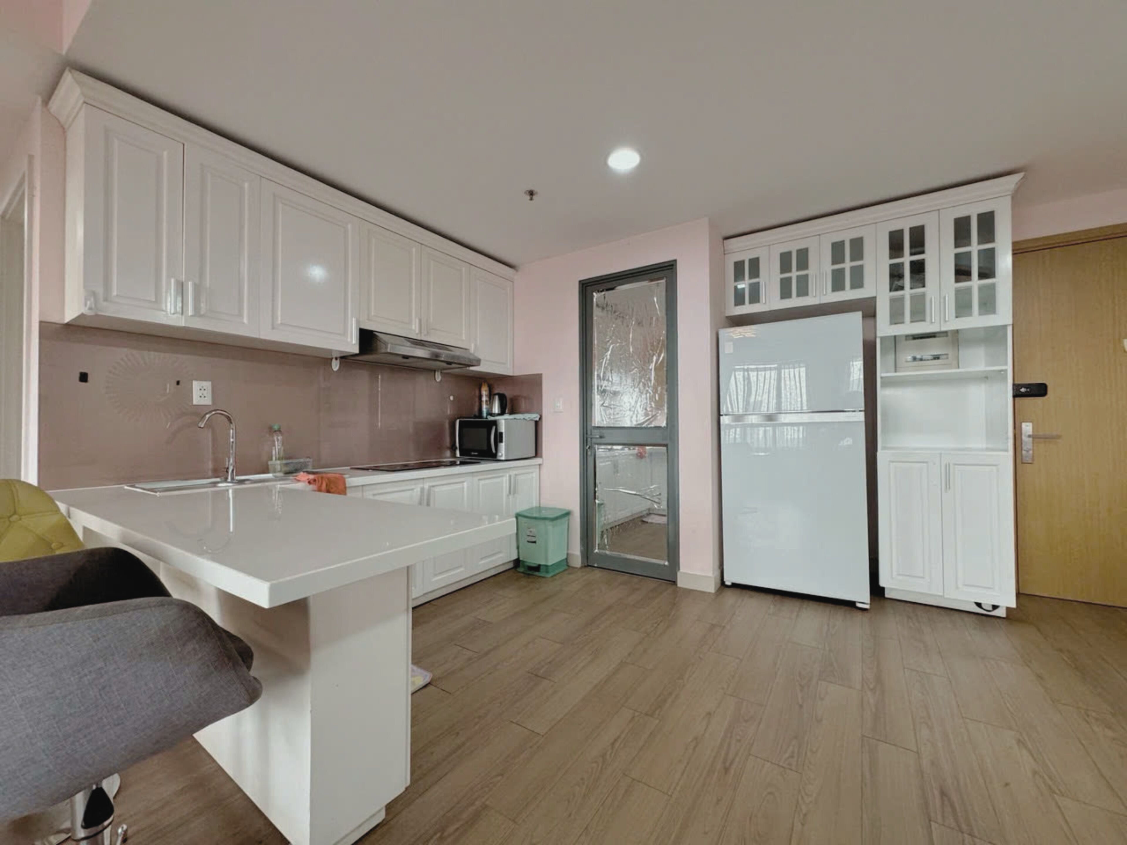 A modern kitchen with white cabinets, a stainless steel range hood, a microwave, and a refrigerator.