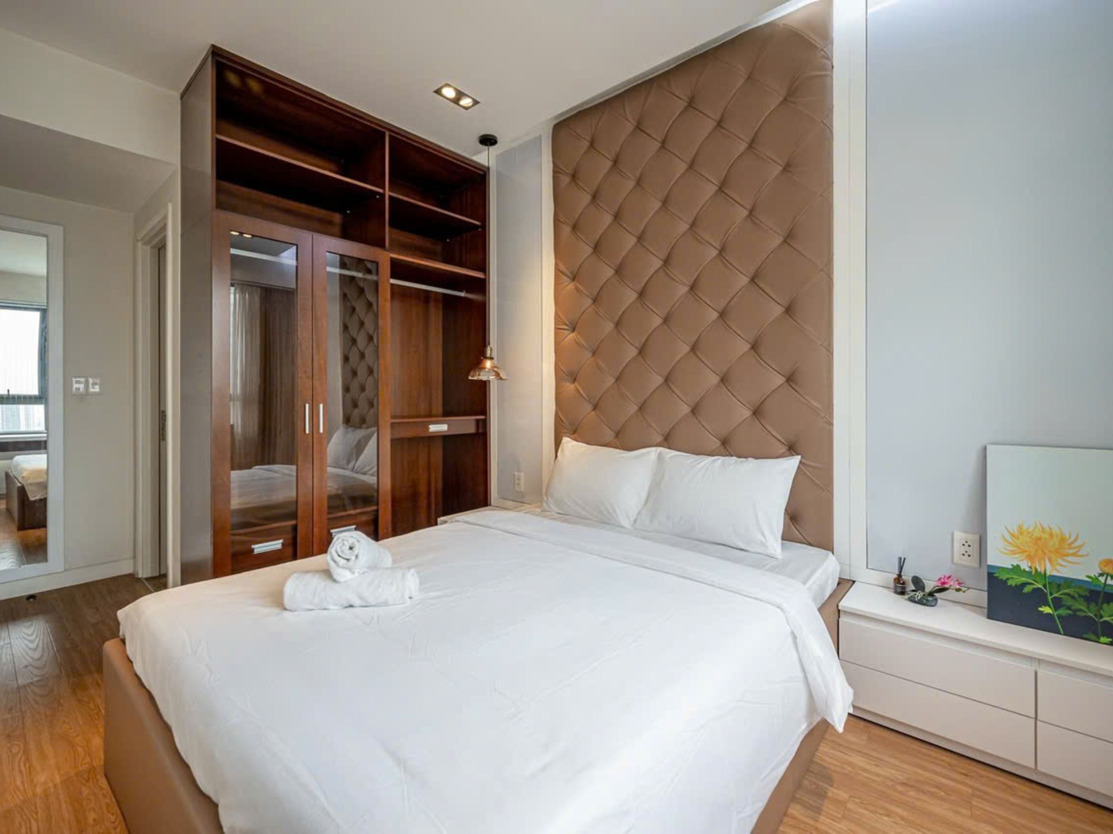 Une chambre d’hôtel avec un grand lit, une armoire en bois, une tête de lit capitonnée et un tableau au mur.