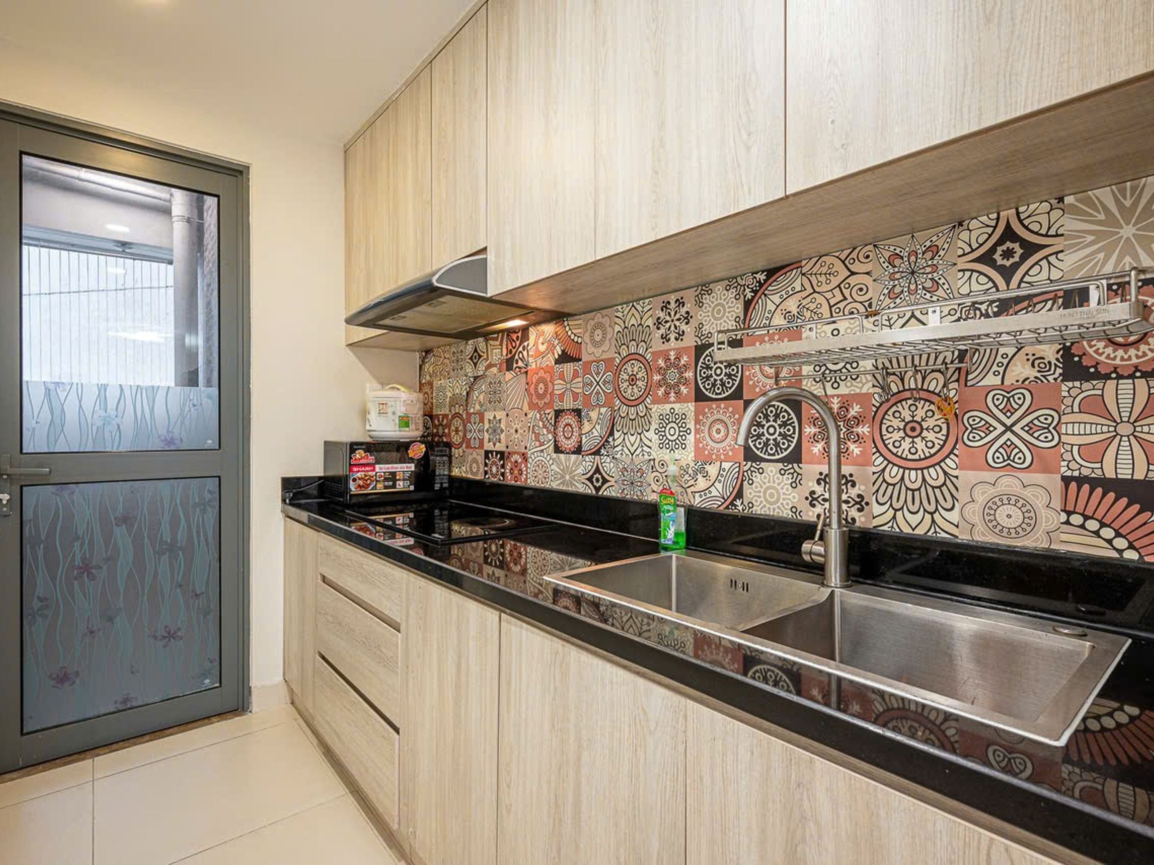 A modern kitchen with wooden cabinets, a black countertop, and a patterned backsplash.
