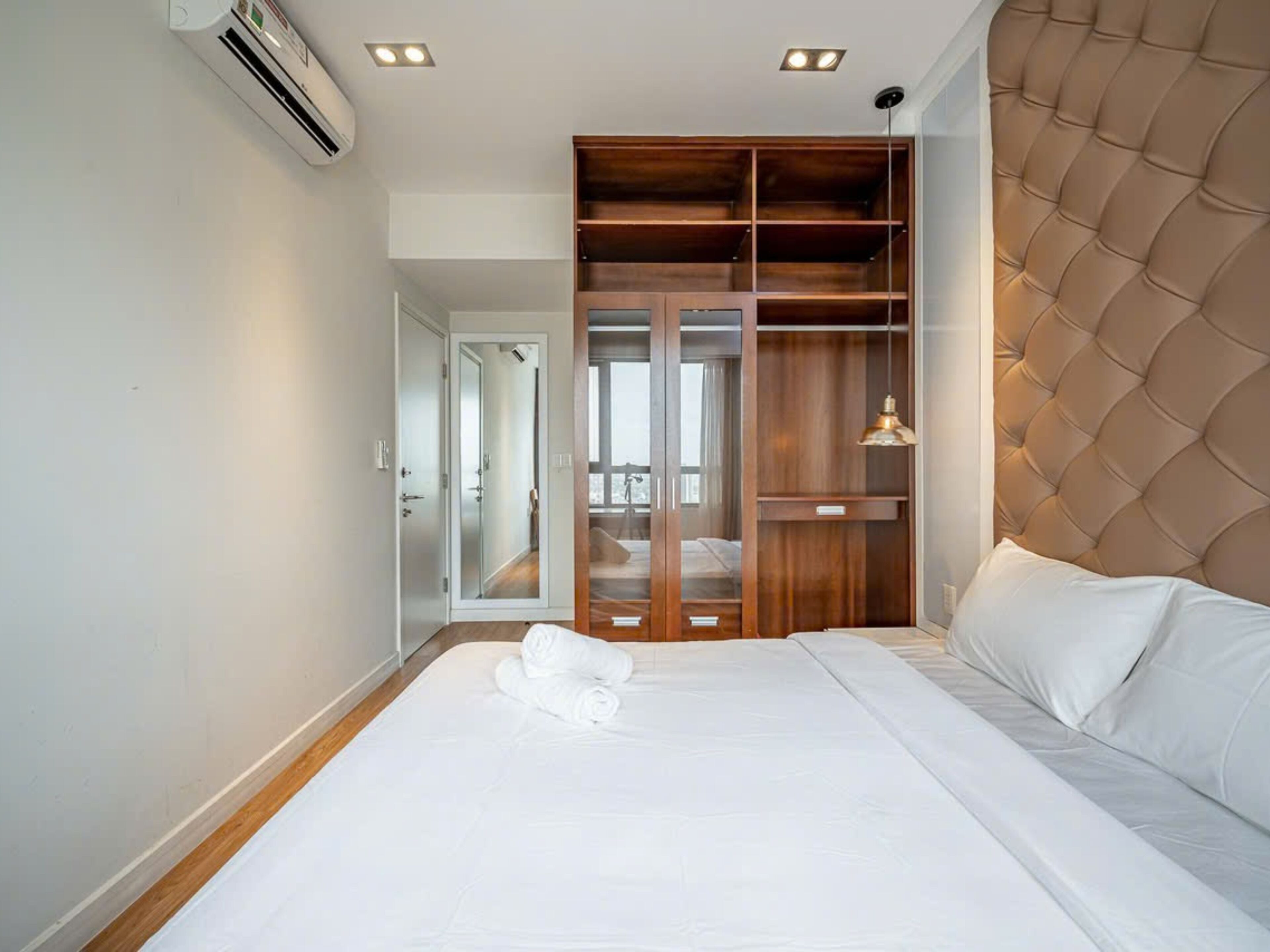 A bedroom with a bed, a wardrobe, and a view of a balcony.
