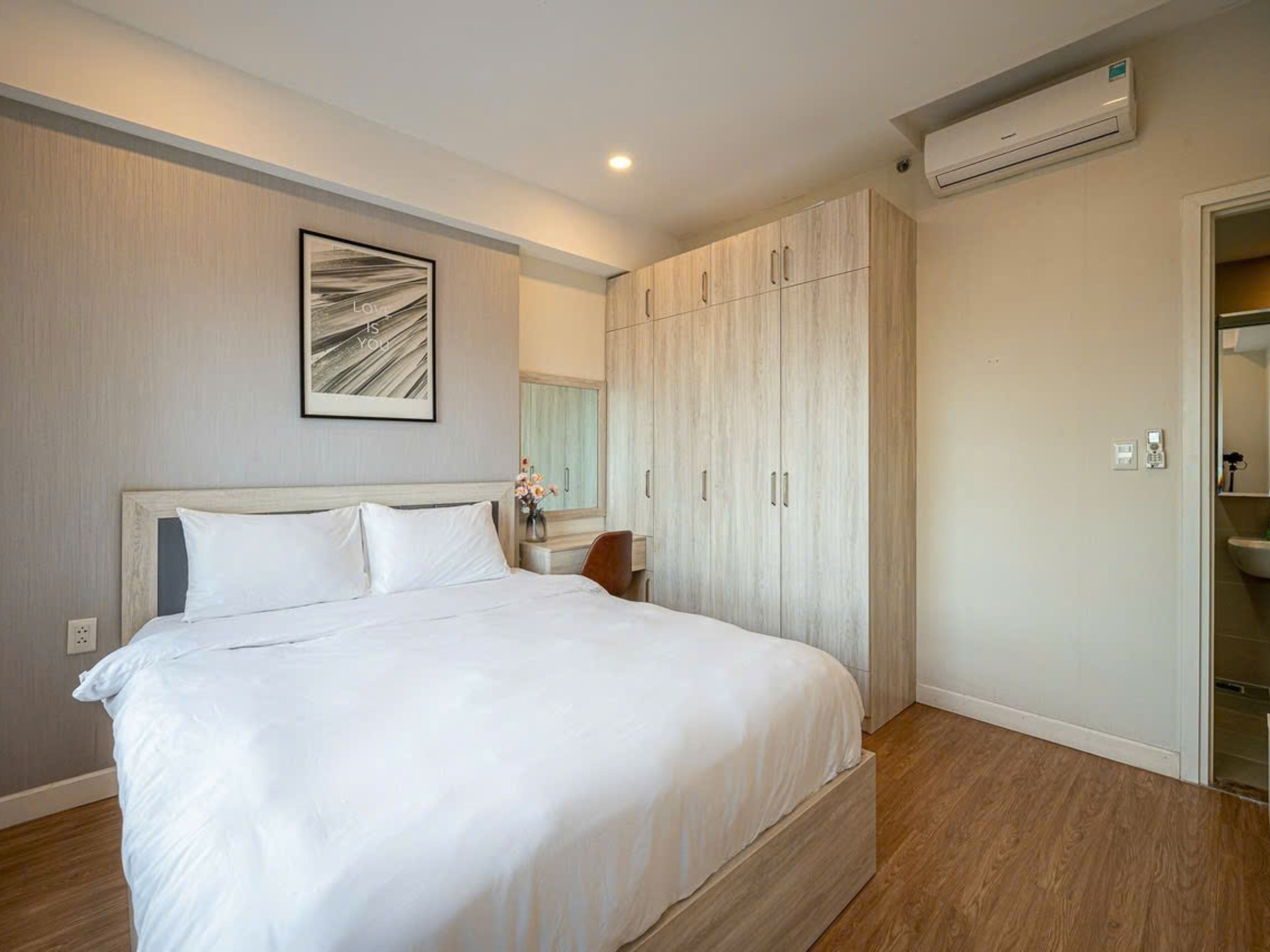 A bedroom with a large bed, wooden wardrobe, and an air conditioning unit.