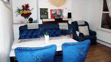 A dining area with a table set for four, blue upholstered chairs, a decorative vase with flowers, a wall clock, and a poster of London.