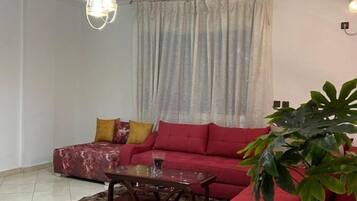 A living room with a red sofa, a coffee table, a potted plant, and a chandelier.