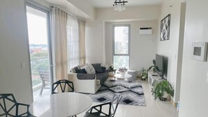 Ein modernes Wohnzimmer mit Essbereich, einer Sofagarnitur, einem Fernseher und Blick auf die Stadt.