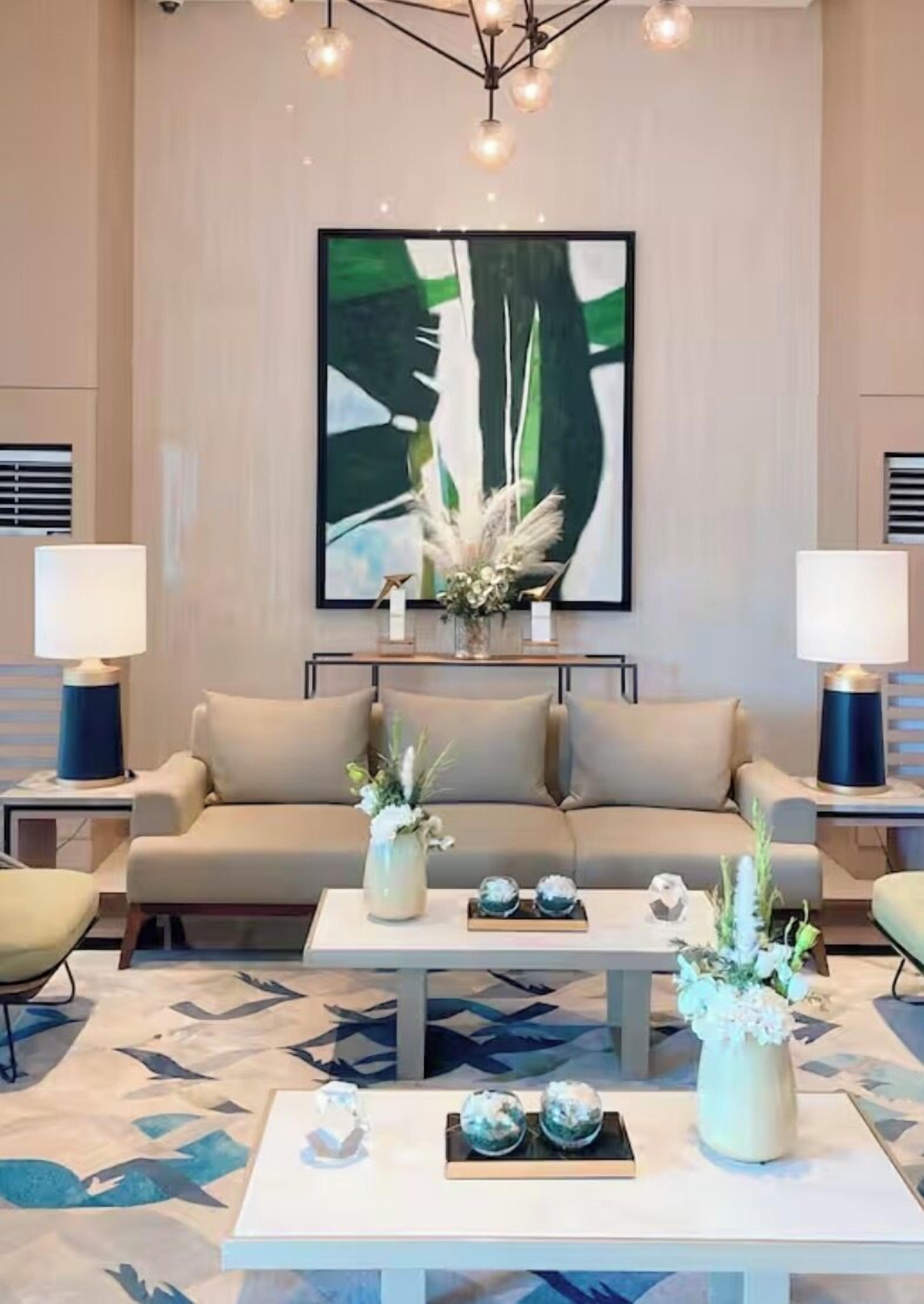 A modern living room with a beige sofa, two side tables with lamps, a coffee table with decorative items, and a large abstract painting on the wall.